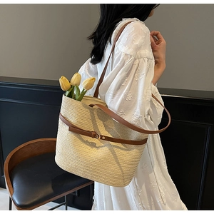 Gros plan d'un sac cabas en paille avec bandoulières en cuir marron porté par un mannequin