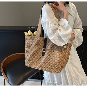 Detail of hand-woven straw tote bag with black leather straps and gold buckle