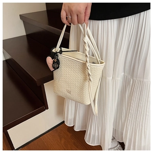 Détail du sac blanc à motif crocodile avec poignée tressée et breloques cœur sur escalier
