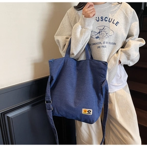 Detail of blue denim tote bag with adjustable shoulder strap and cartoon patch
