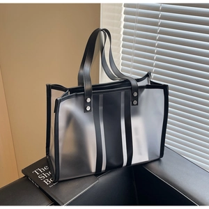 Detail of transparent frosted tote bag with black leather trim on a black leather sofa