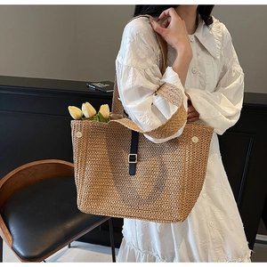 Detail of woven straw tote bag featuring a leather strap and metallic buckle design
