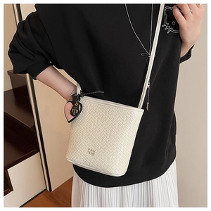 Détail du sac seau tressé en PU crème avec breloques cœur porté par le mannequin