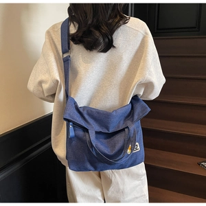 Detail of blue denim tote bag with adjustable strap and cartoon embroidery on a staircase
