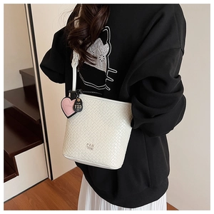 Détail d'un sac seau blanc tressé avec logo embossé et pendentifs décoratifs