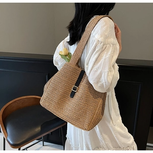 Detail of hand-woven straw tote bag with black leather strap and gold buckle accent