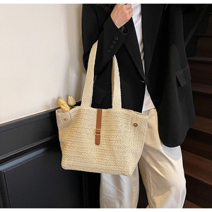 Detail of hand-woven straw tote bag featuring brown leather strap and gold buckle
