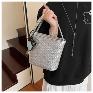 Détail du sac seau tissé argenté avec breloque coeur bleu et poignée porté par mannequin