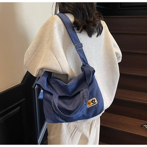 Detail of blue denim tote bag with cartoon patch and adjustable strap worn by model