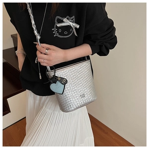 Détail du sac seau en cuir tressé argenté avec logo en métal et pendentif en cœur
