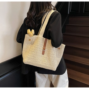 Close-up of woven straw tote bag texture with brown leather strap and metal buckle detail