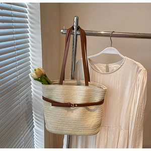 Détail du sac cabas en paille tressée avec lanières en cuir marron et boucles métalliques