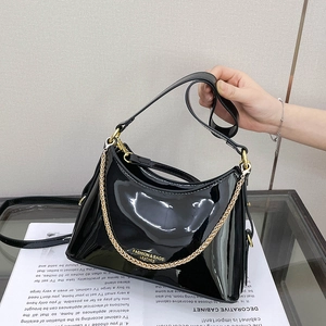 Detail of glossy black patent leather bucket bag with chunky gold chain and fashion logo
