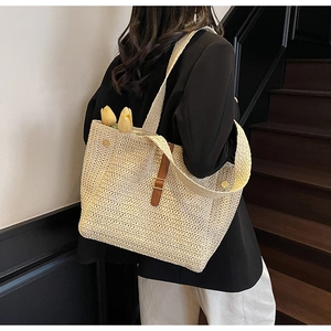 Detailed view of straw woven tote bag featuring brown leather buckle and wide shoulder strap
