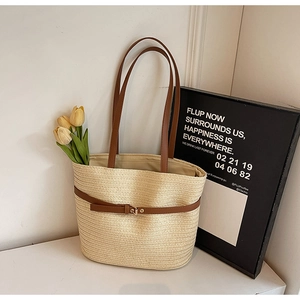 Détail d'un sac cabas en paille tissée beige avec brides en cuir marron et boucle