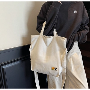 Detail view of cream canvas tote bag with colorful cartoon patch and adjustable straps