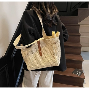 Detail of a large woven straw tote bag with brown leather buckle strap for women