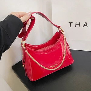 Detail of red patent leather bucket bag with shiny finish and decorative gold chain strap