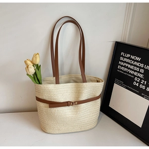 Détail d'un sac cabas en paille tressée avec lanières en cuir marron et boucle en métal