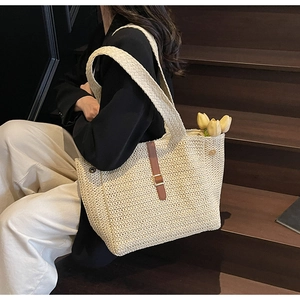 Detail of hand-woven straw tote bag with brown leather accents on wooden stairs