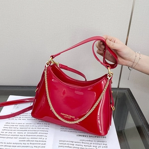 Close-up of bright red patent leather handbag featuring gold chain and fashion lettering