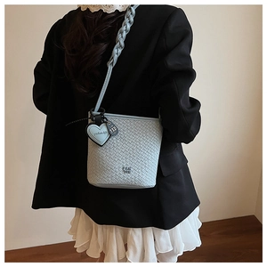 Détail du sac seau tressé bleu clair avec pendentif en cœur et bandoulière tressée