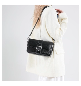 Détail d'un sac sous le bras noir brillant avec boucle argentée sur un tailleur beige