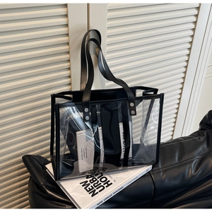 Detailed close-up of transparent PVC tote bag with black leather trim on a sofa