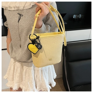 Détail d'un sac seau tressé crème avec breloque en forme de cœur et logo en métal