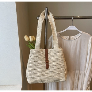 Detail of a woven straw tote bag with brown leather buckle and tulip flower decoration