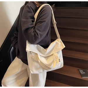 Close-up of a cream canvas tote bag featuring a flap closure and minimalist patch logo
