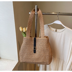 Macro detail of straw woven tote bag featuring black leather straps and gold metal buckles