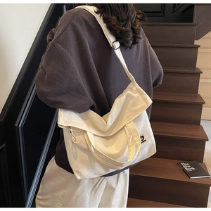 Detail of adjustable strap and square patch on off-white canvas tote bag worn by model