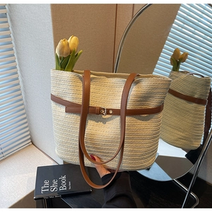 Détail d'un sac cabas en paille tressée avec lanières en cuir marron et boucle élégante