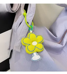 Close-up of yellow plush flower pendant with green beaded strap on a purple bag