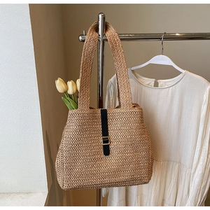Detail of woven straw tote bag featuring black leather strap and gold buckle