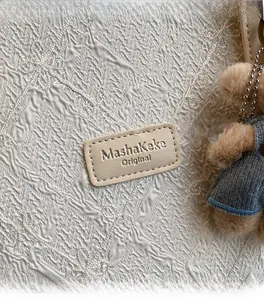 Détail du tissu brodé fleuri avec patch logo en cuir et charmant ours en peluche