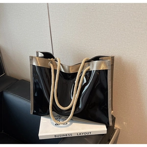 Detail of black patent leather tote bag with gold trim and thick rope handles on a book