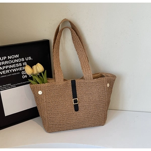 Detail of khaki woven tote bag showing black strap, gold buckle, and refined texture