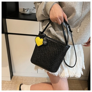 Détail du sac seau tressé noir avec charm cœur jaune et texture de la bandoulière