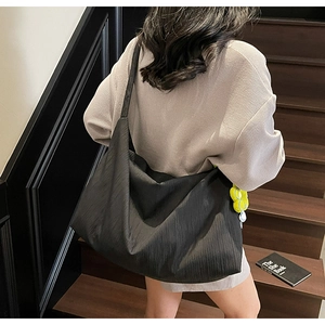 Detail view of large black tote bag with quilted texture and a yellow flower pendant