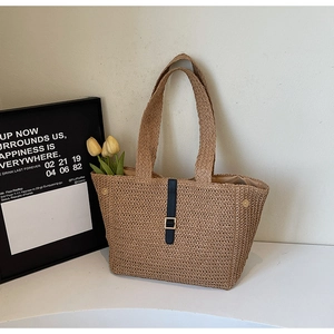 Detail view of woven straw tote bag featuring black leather straps and gold buckle accent