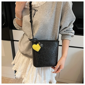 Détail du sac seau tressé noir avec breloque cœur jaune et longue bandoulière