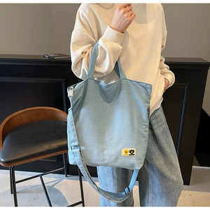 Detail of light blue canvas tote bag featuring adjustable strap and cute character patch