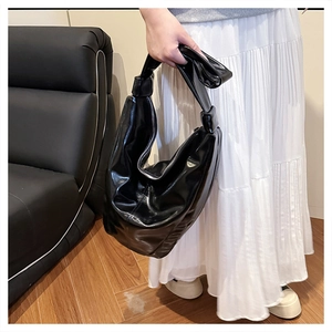 Détail du sac hobo noir brillant avec bandoulière nouée et finition vernie élégante