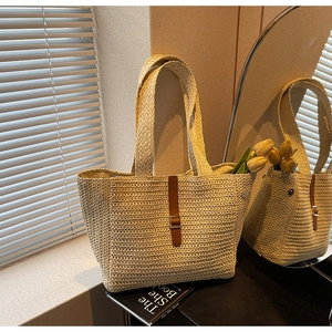 Detail of beige woven tote bag with brown leather strap and silver metal buckle