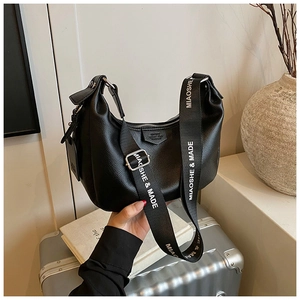 Gros plan du sac hobo noir en cuir grainé avec bandoulière imprimée sur une valise