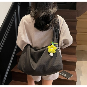 Detail of a black large capacity tote bag with a yellow flower charm and webbing strap