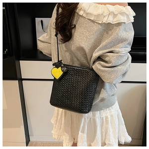 Détail d'un sac bandoulière noir tressé avec un pendentif en cuir en forme de cœur jaune