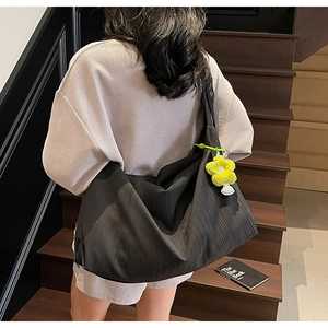 Detail of black pleated fabric tote bag with a bright yellow flower charm on a wide strap